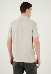 Kurzarm-Polohemd in einem hellbeigen Farbton mit klassischem Kragen, glatter Textur und sauberem Nähen. Getragen mit dunkelgrauen Jeans.