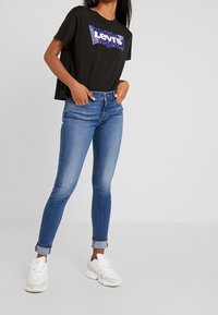 Svart kortärmat T-shirt med en färgglad Levi's-logga, i kombination med ljusblå skinny jeans och vita sneakers med detaljer.