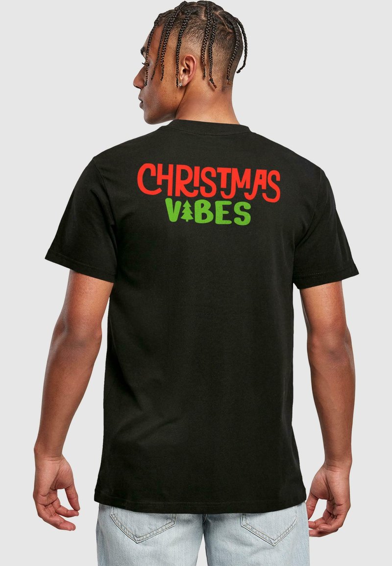 Black cotton T-shirt featuring the text "CHRISTMAS VIBES" in red and green with a Christmas tree icon, seen from the back.