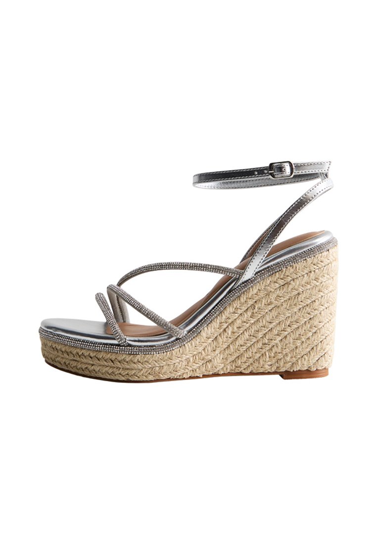 Silver wedge sandal with braided rope heel, metallic straps, and a textured, glossy sole. Ankle strap with buckle detail.