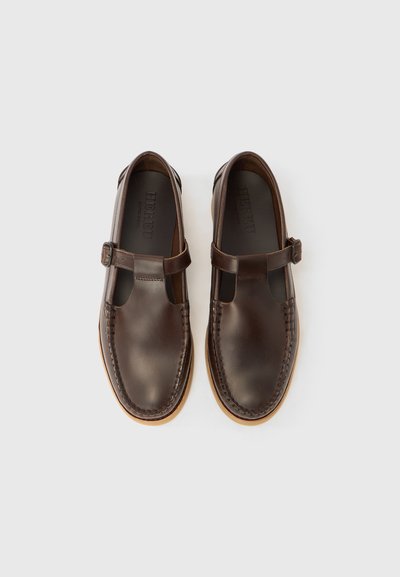 Καφέ δερμάτινα παπούτσια με στρογγυλεμένη μύτη, λουράκι τύπου Τ και διακοσμητικό ράψιμο. Φωτεινή καφέ σόλα και ομαλή υφή σε όλο το παπούτσι.