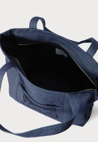 Τσάντα tote από τζιν σε σκούρο μπλε με υφή στην εξωτερική πλευρά που διαθέτει ανάγλυφο σχέδιο. Το εσωτερικό είναι μαύρο, με κλείσιμο με φερμουάρ και διπλές λαβές.