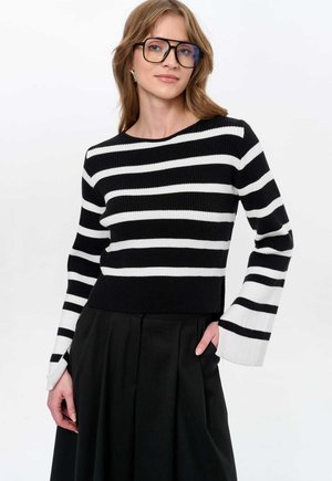 Schwarz-weißer gestreifter Strickpullover mit langen Glockenärmeln, kombiniert mit einem schwarzen Plisseerock. Glatte Textur, Rundhalsausschnitt, moderner Schnitt.