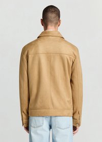 Beige Wildlederjacke mit weicher Textur, klassischem Kragen, großer Rückennaht und geknöpften Manschetten, kombiniert mit hellblauen Jeans.