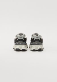 Scarpe da ginnastica nere e grigie con una parte superiore testurizzata, colletto imbottito e design della suola bianca ondulata. Presentano il logo sul tallone.