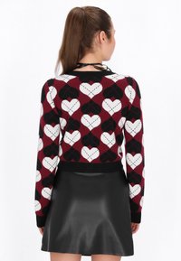 Maglione lavorato a maglia con un motivo a cuore in rosso, bianco e nero. Design aderente con un orlo a coste neri. Abbinato a una gonna nera in pelle.