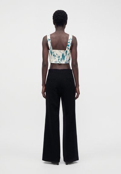 Femme vue de dos portant un crop top sans manches bleu et blanc et un pantalon noir large taille haute sur un fond uni.