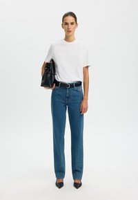 Witte katoenen t-shirt, blauwe rechte jeans, zwarte leren handtas en zwarte puntige hakken. Eenvoudig ontwerp en casual pasvorm.