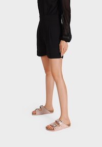 Infradito rosa chiaro e beige con due fibbie metalliche regolabili, plantare in sughero e suola testurizzata. Indossati con pantaloni neri.