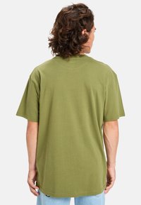 Olivově zelené bavlněné tričko s krátkými rukávy a volným střihem, s kulatým výstřihem a rovným lemem. Není vidět žádný vzor ani hardware.