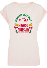 Ljusrosa kortärmad t-shirt med ett grafiskt tryck av "Säsongens hälsningar från Upside Down", med grön och röd text samt juliga detaljer.