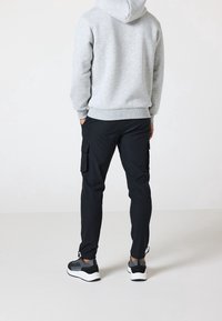 Felpa grigia con tasca frontale, abbinata a pantaloni cargo neri con tasche laterali e scarpe da ginnastica nere con suole bianche.