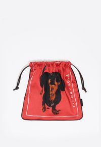 Czerwony woreczek ze sznurkiem z ilustracją czarno-brązowego jamnika, obrysowanego na biało, z brązowymi akcentami sznurka na górze.