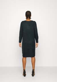 Mörkgrön stickad klänning med långa ärmar, rund halsringning och längd till mitt på vadden, med en slät yta och sidslitsar.