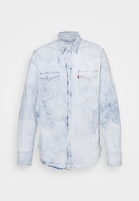 Camicia di jeans azzurro chiaro con una texture sbiadita, chiusura con bottoni a scatto, due tasche sul petto, dettagli della yoke a punta e maniche lunghe.