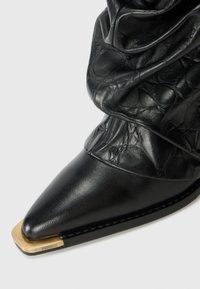Black leather pointed-toe boot with slouched shaft and gold metal toe cap detail embossed with "BRONX" on a white background.
