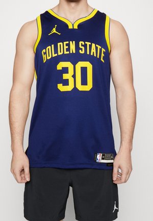 Homme portant un maillot de basketball Golden State de couleur bleu marine avec le numéro 30 en jaune et un short noir avec le logo de la marque Jordan.