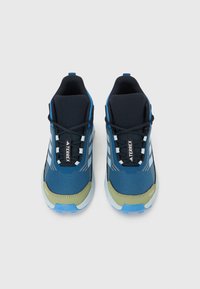 Ζευγάρι από μπλε και μαύρα αθλητικά παπούτσια Adidas Terrex με μπεζ άνω μέρος στα δάχτυλα και λευκές σόλες, φαίνονται α πό ψηλά σε λευκό φόντο.