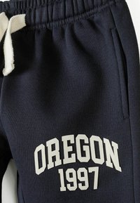 Mörkblå mjukisbyxor med en plyschtextur, med en vit dragsko och tryckt "OREGON 1997" i fet, off-white lettering.