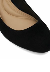 Chaussure plate en suède noir avec un bout arrondi et un intérieur beige lisse. La semelle extérieure est plate et offre un design simple et minimaliste.