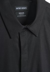 Camisa negra de cuello hecha de una mezcla de algodón de tacto suave. Presenta un corte regular con etiquetas de marca visibles: "ANTONY MORATO" y "DENVER."