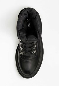 Botín negro hasta el tobillo con exterior de cuero liso, cuello acolchado, ojales plateados y cordones. Suela texturizada para tracción y estabilidad.