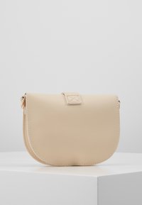 Beige läderhandväska med rundad form, tryckknappsöppning och subtila sömnadsdetaljer. Små guldfärgade detaljer.