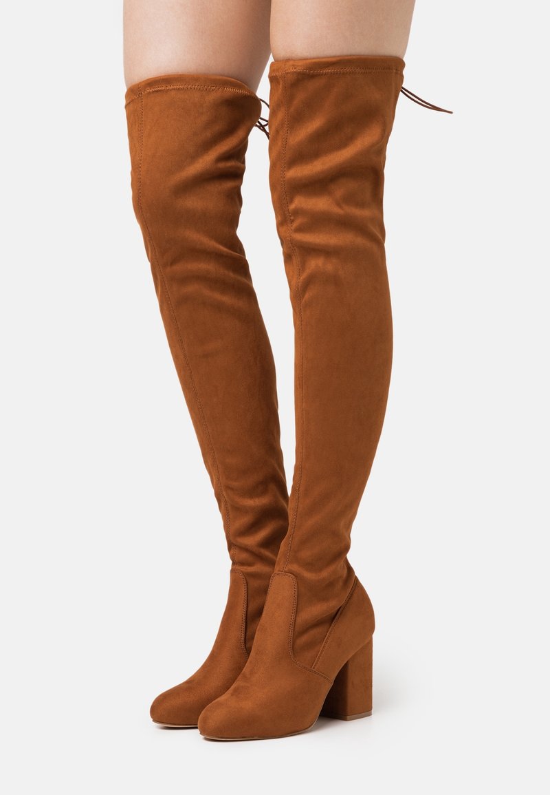 Botas de ante marrón por encima de la rodilla con tacón de bloque estructurado. Textura suave, diseño ajustado y detalle de cordones en la parte superior.