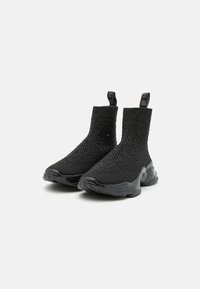 Une paire de baskets montantes noires en maille, avec une semelle texturée et des languettes de traction, sur fond blanc.