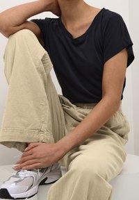 Marinblå kortärmad t-shirt, krämfärgade texturerade vida byxor och vita mesh sneakers med silverdetaljer. Diskreta sömmar och avslappnad passform.