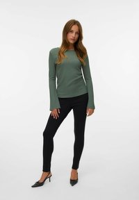 Grön långärmad topp med texturerat tyg, matchad med svarta slim-fit byxor och svarta klackskor.