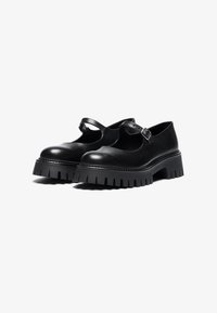 Black leather shoes with a rounded toe, a cutout design, and an adjustable ankle strap. Features a thick, ridged sole for added traction.
