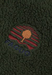 Tessuto in pile verde con superficie texturizzata. Presenta un logo ricamato in tonalità di rosso e marrone, che raffigura un albero e strisce. Il testo dice "FAGUO."