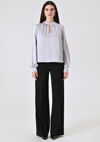Blusa in satin grigio chiaro con scollatura a chiave, maniche lunghe a sbuffo e vestibilità comoda, abbinata a pantaloni neri a gamba larga.