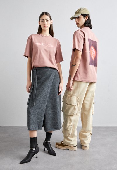 Pink logo t-shirt, grey wrap skirt with tie, black heeled boots, beige cargo pants, and tan chunky shoes, minimalist design and textures.
