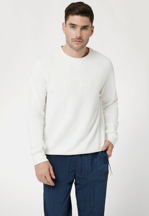 Hvid sweatshirt med præget "GUESS" logo, ribbede manchetter og rund halsudskæring. Kombination med navy blå strukturerede bukser.