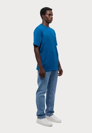 Blå bomulls T-skjorte med korte ermer, kombinert med lys blå jeans og hvite joggesko. T-skjorten har en klassisk passform og myk tekstur.