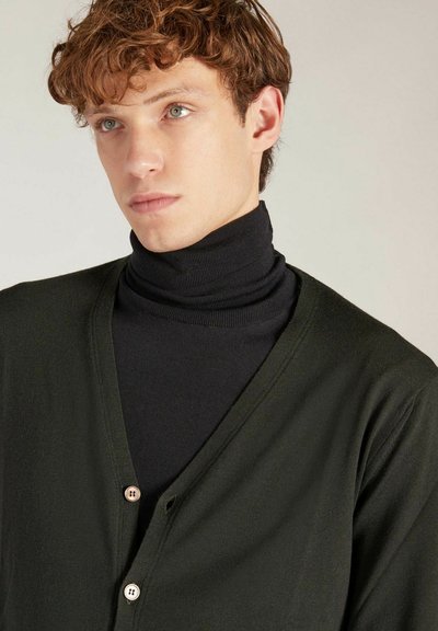 Gilet vert foncé avec un design en V, comportant deux boutons à l'avant, superposé sur un col roulé noir. Texture douce visible dans le tissu.