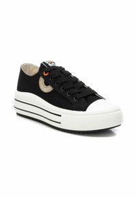 Zapatillas de lona negras con una puntera de goma blanca y suela a rayas en blanco y negro. Presentan acentos texturizados y un detalle de logo circular.