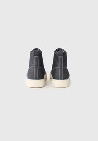 Høye sneakers i mørk denim med hvite sømmer, teksturert gummisåle og kontrasterende beige detaljer ved bunnen og baksiden.