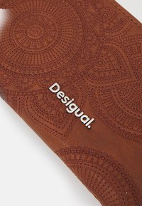 Braune Lederbörse mit geprägten kreisförmigen Mustern und einem silbernen "Desigual"-Logo. Structurierte Oberfläche, glatte Kanten und rechteckige Form.