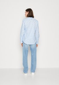 Camicia button-up azzurro chiaro con motivo a foglie bianche, abbinata a pantaloni in denim chiaro. Presenta maniche lunghe e un orlo curvo.