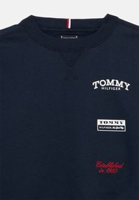 Granatowa bluza crewneck z logo Tommy Hilfiger i napisem "Established in 1985" czerwonym pismem na przodzie.