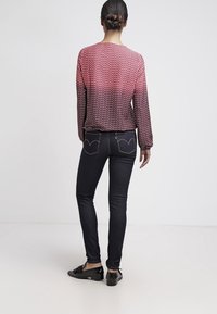 Blusa a maniche lunghe con motivo in rosso e blu navy, abbinata a jeans skinny scuri con tasche posteriori a forma di cuore e scarpe slip-on nere.