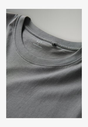 T-shirt grigia in cotone a girocollo steso, con colletto cucito e etichetta interna stampata con dettagli sul marchio e sulla taglia.
