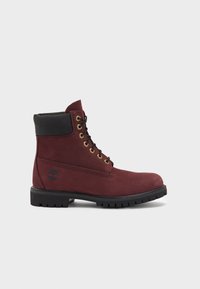 Bordeaux Suede-Ankleboot mit schwarzem Lederkragen, goldenen Ösen, schwarzen Schnürsenkeln und einer strukturierten Gummisohle mit einem ausgeprägten Profil.