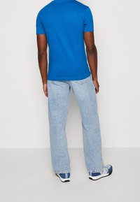 Modré bavlněné tričko s krátkým rukávem; nošeno s světle modrými džíny s rovnými nohavicemi a modrými sportovními botami s bílými detaily a logem.