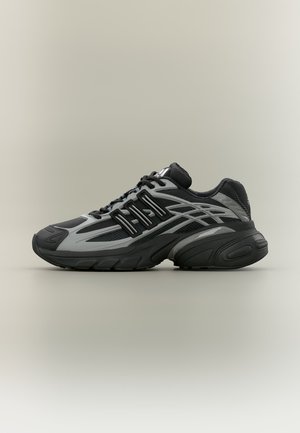 Sneaker atletica nera e grigia con tomaia in mesh, suola spessa e design con lacci neri, mostrata dal lato esterno su sfondo semplice.