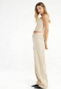 Beige, glanzend cropped top met een vierkante halslijn, gecombineerd met hooggesneden, wijde broekspijpen met een subtiele textuur en een getailleerd silhouet.
