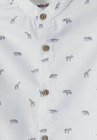 Vit skjorta med knappar som har små svarta djursiluetter, inklusive tigrar och giraffer, med bruna knappar och en krage.